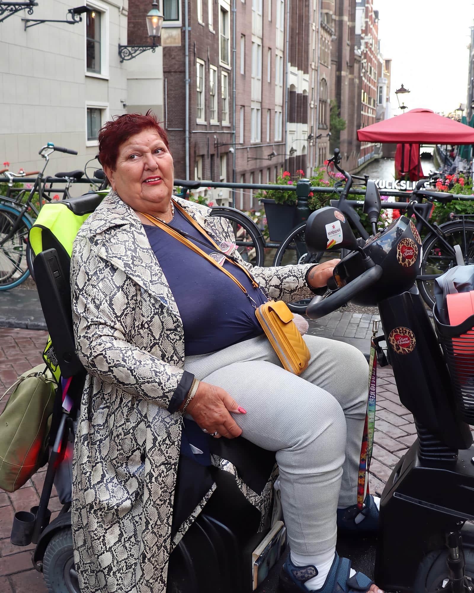 Lida op haar scootmobiel bij de Kolksluis, in slangenprintjas, met de gracht achter haar