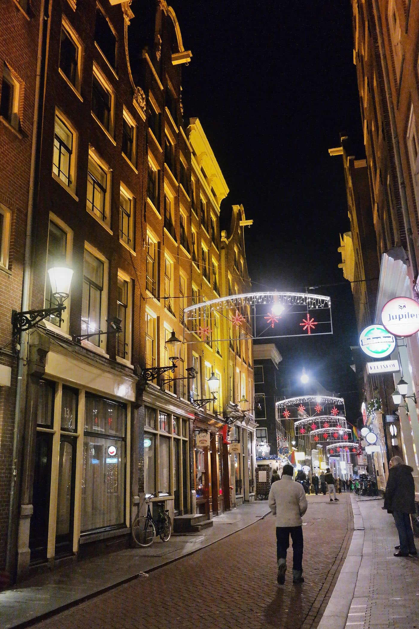 De Zeedijk bij avond, met lantaarns, verlichte gevels en een paar voorbijgangers op de klinkers