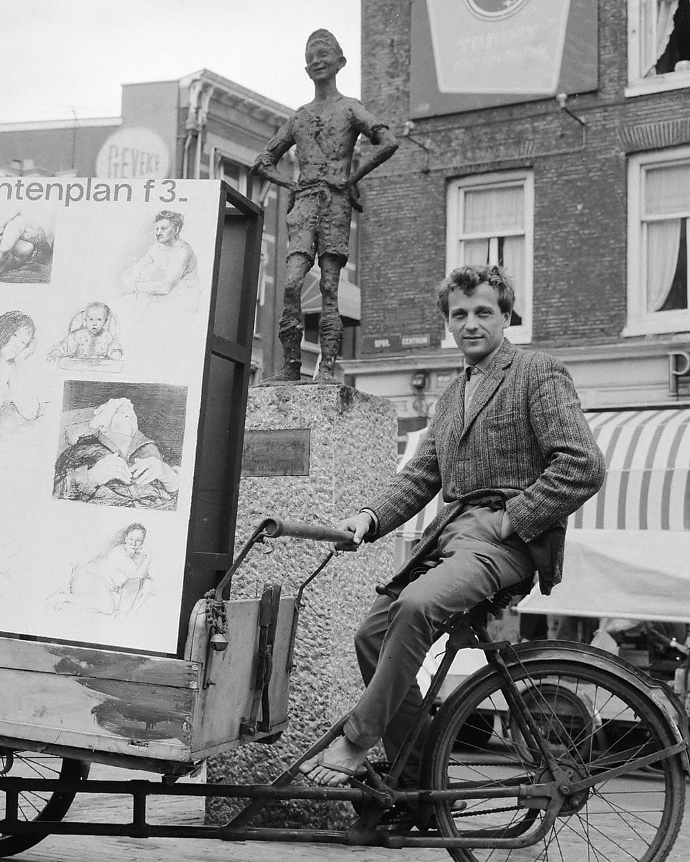 Zwart-witfoto uit 1964: Robert Jasper Grootveld op zijn bakfiets met tekeningen op het Spui, met Het Lieverdje achter hem